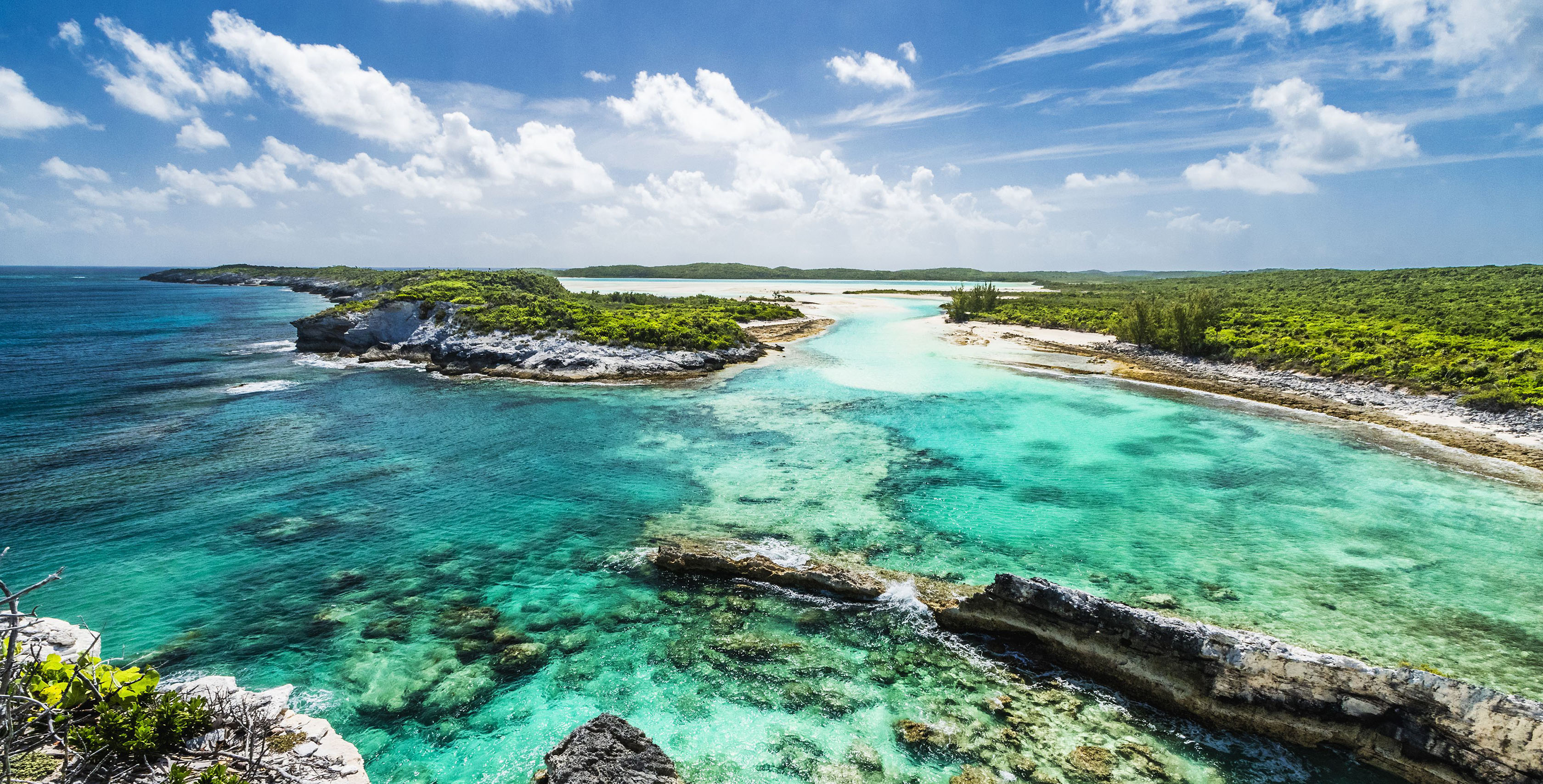 Bright green sea water with rocks with blue sky and white clouds