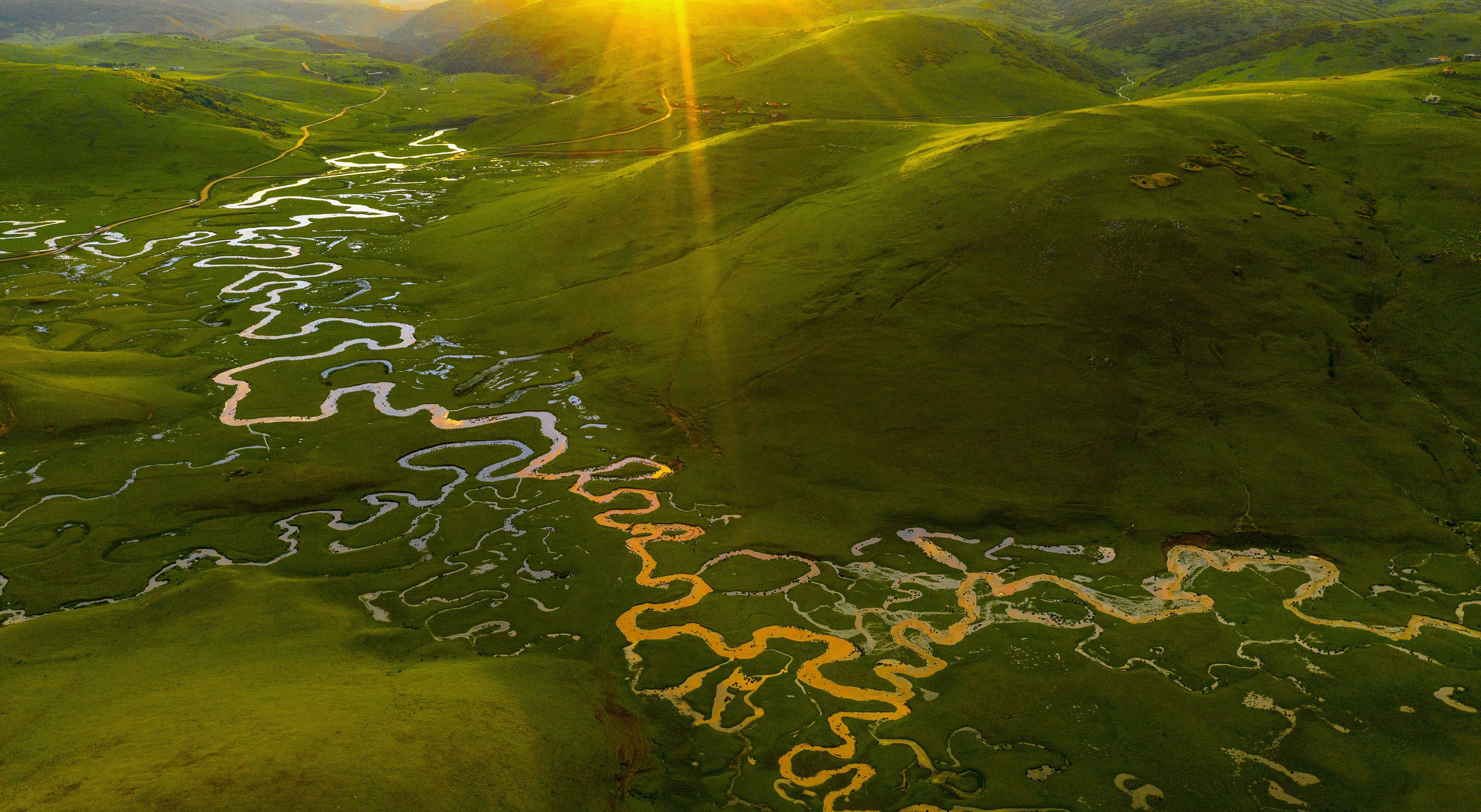 Top view of river between green hills with sun beams at top right