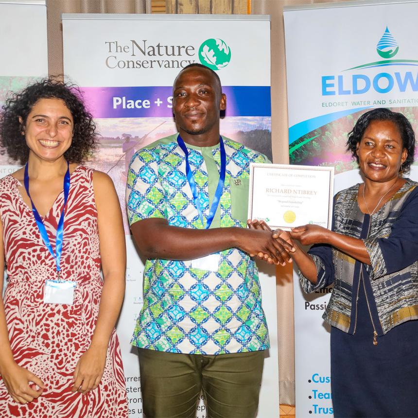 Man (middle between two women) receives training certificate