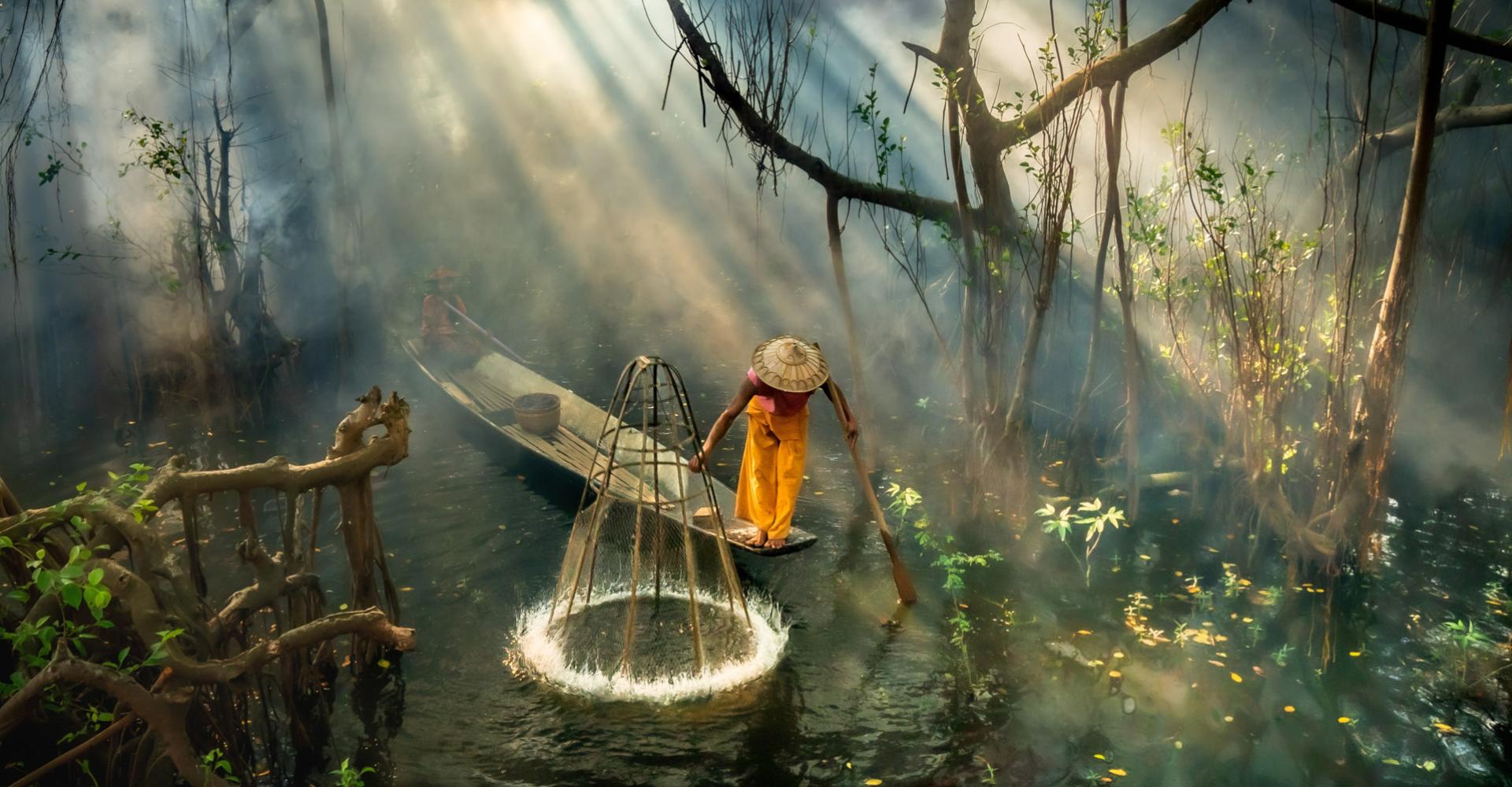 Fisherman standing is small canoe in middle of jungle river
