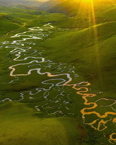 Top view of river between green hills with sun beams at top right